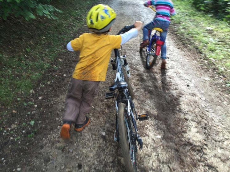 Kind schiebt Fahrrad im Wald beim Fahrradkurs für Kinder