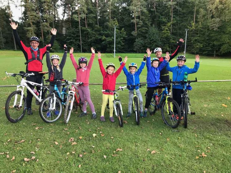 Kinder und Trainer heben die Hände hoch beim Fahrradkurs für Kinder