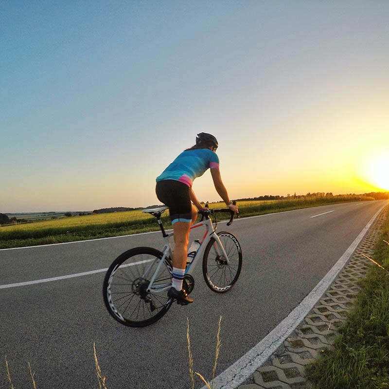 Frau fährt mit Rennrad entgegen Sonnuntergang